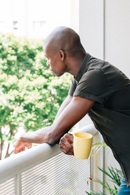Portret młody człowiek trzyma filiżankę kawy w ręce patrzeje na zewnątrz balkonu