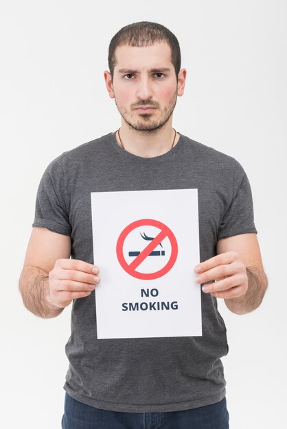 Portret młody człowiek trzyma palenie zabronione szyldową pozycję przeciw białemu tłu