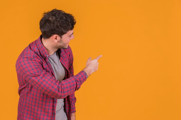 Portret młody człowiek wskazuje jego palec i patrzeje pomarańczowego tło