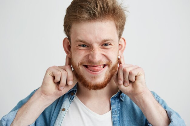 Portret młody rozochocony wesoły facet robi śmiesznej twarzy oszukiwać pokazuje jęzor.