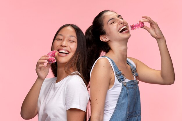 Portret młodych nastoletnich dziewcząt pozujących razem i jedzących pączki