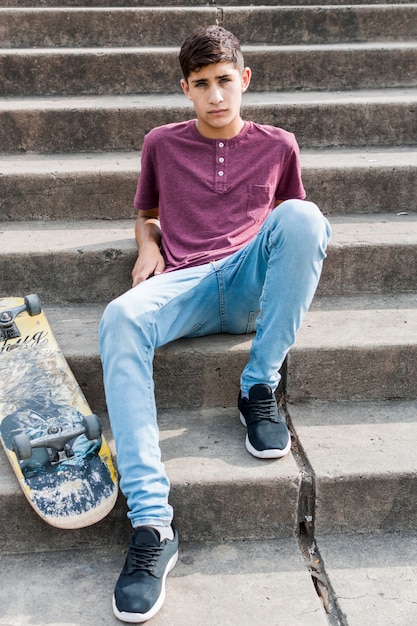 Portret nastoletni chłopak siedzi na betonowym schody z deskorolka