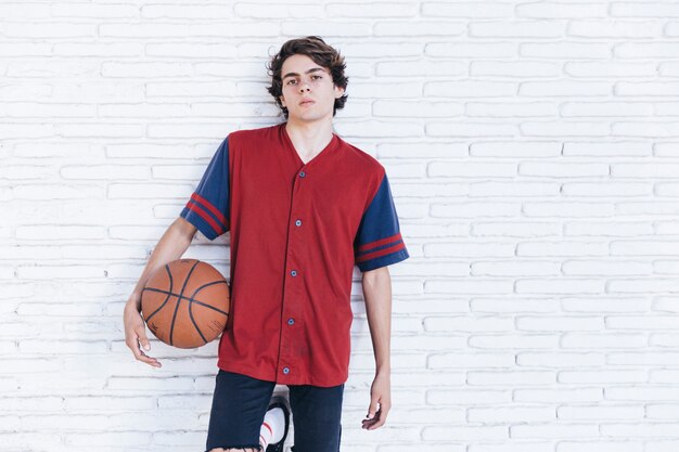 Portret nastoletni chłopak z koszykówką opiera na ściana z cegieł