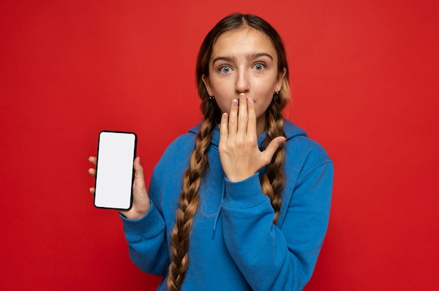 Bezpłatne zdjęcie portret nastoletniej dziewczyny pokazującej smartfona i wyglądającej na zaskoczoną