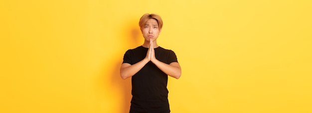 Portret nieszczęśliwego azjatyckiego faceta błagającego o pomoc stojącego na żółtym tle