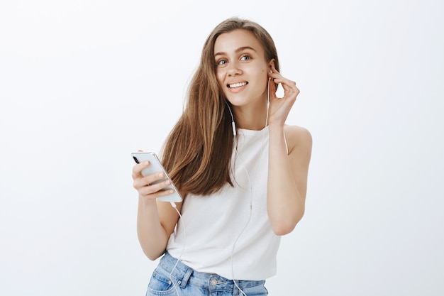 Portret nowoczesnej atrakcyjnej dziewczyny umieścić słuchawki, słuchając podcastów lub muzyki na telefonie komórkowym