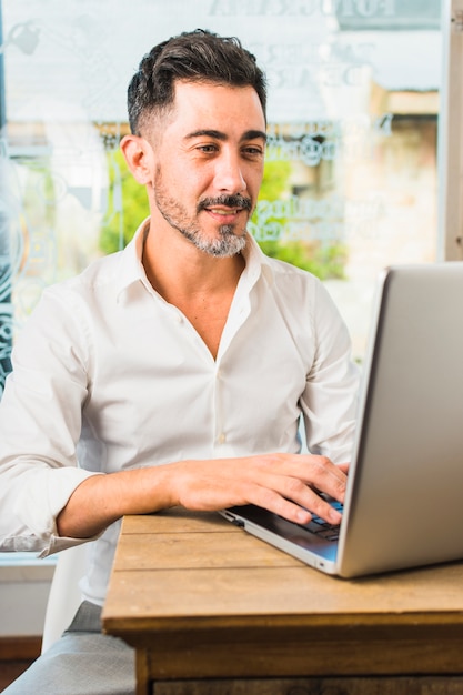 Portret nowożytny mężczyzna obsiadanie w cukiernianym używa laptopie