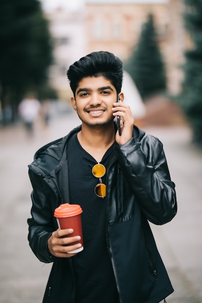 Portret opowiada na telefonie i chodzi na ulicie młody człowiek