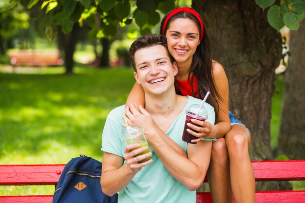 Portret pary obsiadanie na ławki mienia smoothies w plastikowej filiżance