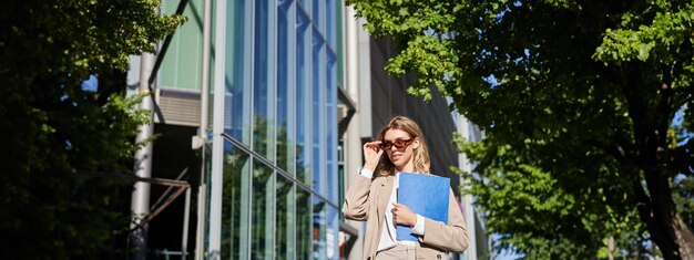 Bezpłatne zdjęcie portret pewnej siebie korporacyjnej kobiety idącej do biura z teczką chodzącej po ulicy w słoneczny dzień