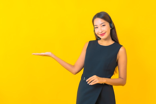 Portret piękna młoda azjatycka biznesowa kobieta z obsługą klienta call center zestawu słuchawkowego na żółtym tle