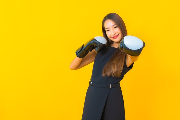 Portret piękna młoda azjatycka biznesowa kobieta z rękawicą bokserską na żółtym tle