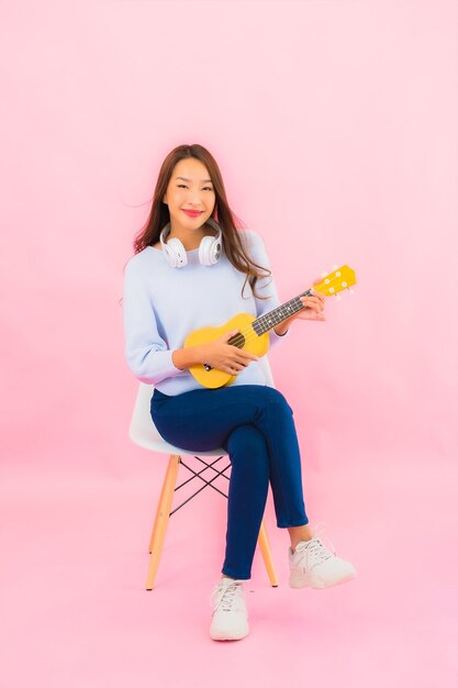 Portret piękna młoda azjatycka kobieta gra na ukulele na różowej ścianie na białym tle