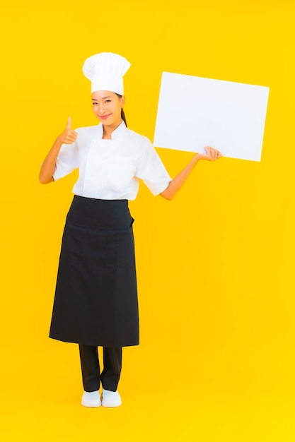 Portret piękna młoda azjatycka kobieta szefa kuchni z białym pustym billboardem na żółtym tle na białym tle