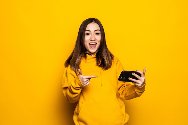 Portret piękna młoda azjatycka kobieta uśmiech szczęśliwego korzystania z inteligentnego telefonu komórkowego na żółtej izolowanej ścianie