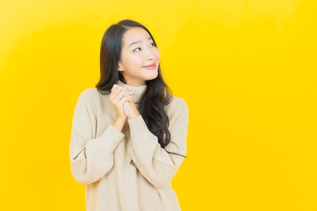 Portret piękna młoda azjatycka kobieta uśmiecha się z akcją na żółtej ścianie