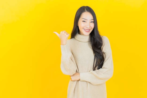 Portret piękna młoda azjatycka kobieta uśmiecha się z akcją na żółtej ścianie