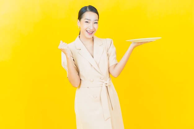 Portret piękna młoda azjatycka kobieta uśmiecha się z pustym talerzem na kolorowej ścianie