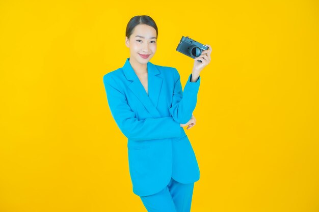 Portret piękna młoda azjatycka kobieta używa aparatu na żółto