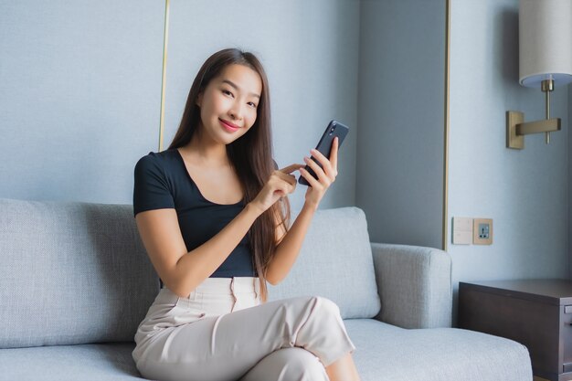 Portret piękna młoda azjatycka kobieta używa inteligentnego telefonu komórkowego na kanapie w salonie