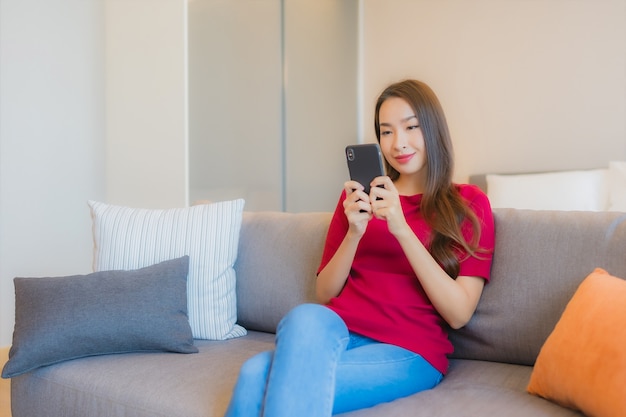 Portret piękna młoda azjatycka kobieta używa inteligentnego telefonu komórkowego na kanapie