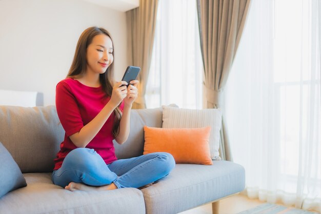 Portret piękna młoda azjatycka kobieta używa inteligentnego telefonu komórkowego na kanapie