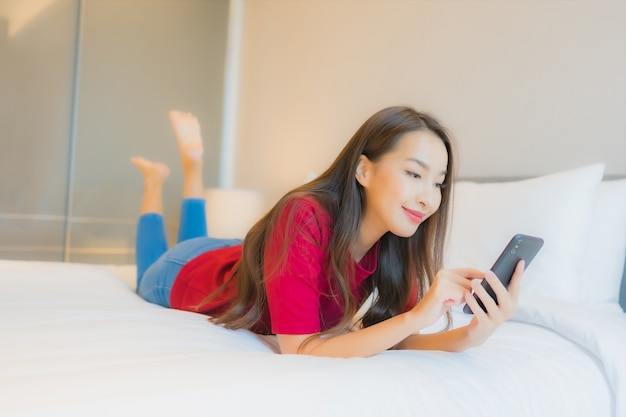 Portret piękna młoda azjatycka kobieta używa inteligentnego telefonu komórkowego na łóżku
