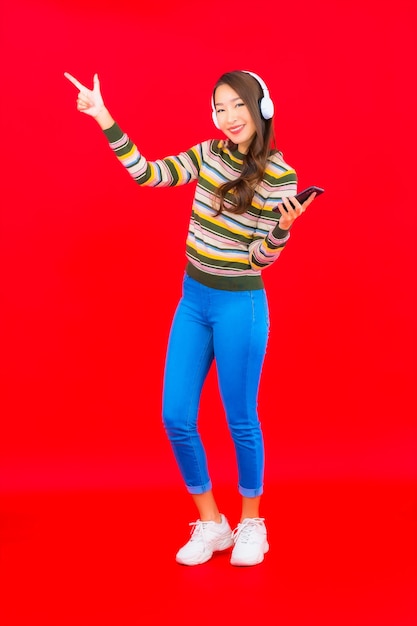Portret piękna młoda azjatycka kobieta używa inteligentnego telefonu komórkowego z słuchawkami do słuchania muzyki