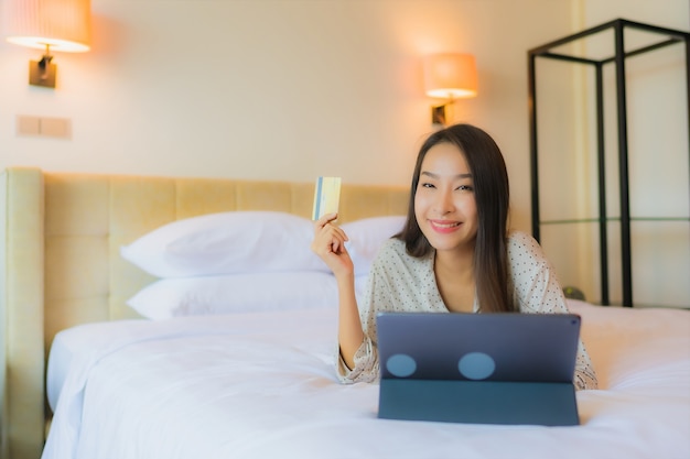 Portret piękna młoda azjatycka kobieta używa tabletu z kartą kredytową na łóżku