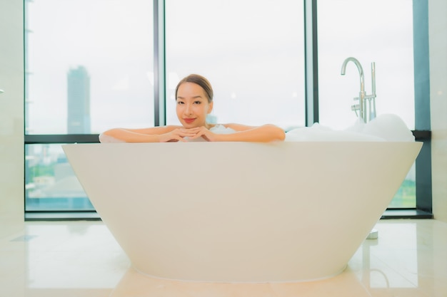 Portret piękna młoda azjatycka kobieta zrelaksować się uśmiech wypoczynek w wannie we wnętrzu łazienki