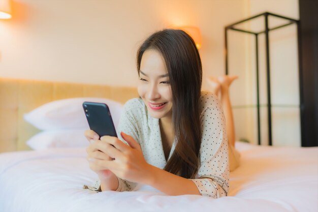 Portret piękna młoda azjatykcia kobieta na łóżku z inteligentny telefon komórkowy