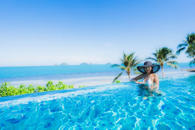 Portret piękna młoda azjatykcia kobieta relaksuje w luksusowym plenerowym pływackim basenie w hotelowego kurortu prawie plażowym dennym oceanie