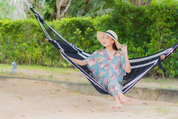 Bezpłatne zdjęcie portret piękna młoda azjatykcia kobieta siedzi na hamaku huśtawka wokół oceanu plaży na wakacjach