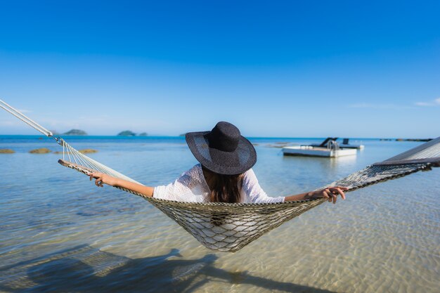 Portret piękna młoda azjatykcia kobieta siedzi na hamaku wokoło dennej plaży oceanu dla relaksu