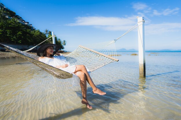 Portret piękna młoda azjatykcia kobieta siedzi na hamaku wokoło dennej plaży oceanu dla relaksu