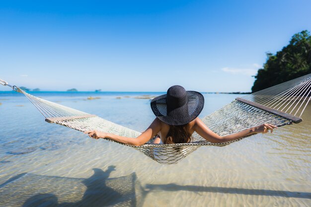 Portret piękna młoda azjatykcia kobieta siedzi na hamaku wokoło dennej plaży oceanu dla relaksu