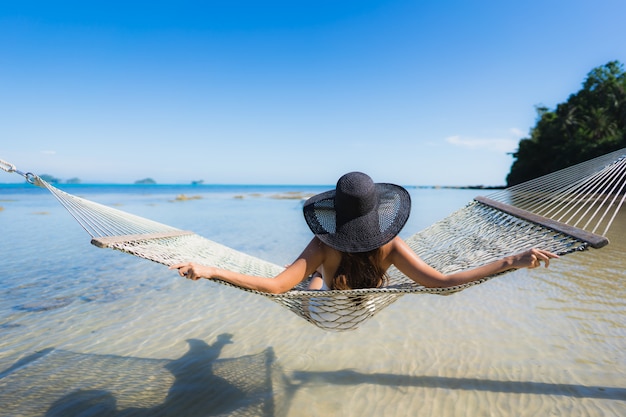 Portret piękna młoda azjatykcia kobieta siedzi na hamaku wokoło dennej plaży oceanu dla relaksu