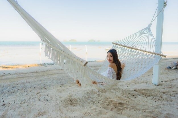 Portret piękna młoda azjatykcia kobieta siedzi na hamaku wokoło dennej plaży oceanu dla relaksu