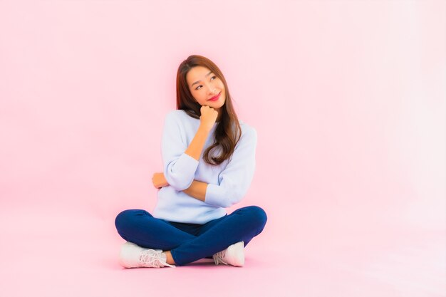 Portret piękna młoda azjatykcia kobieta siedzi na podłodze z różową ścianą na białym tle