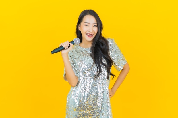 Portret piękna młoda azjatykcia kobieta śpiewa piosenkę z mikrofonem na żółto