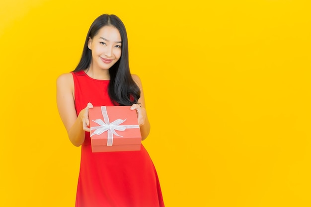 Portret piękna młoda azjatykcia kobieta uśmiech z czerwonym pudełkiem na żółtej ścianie