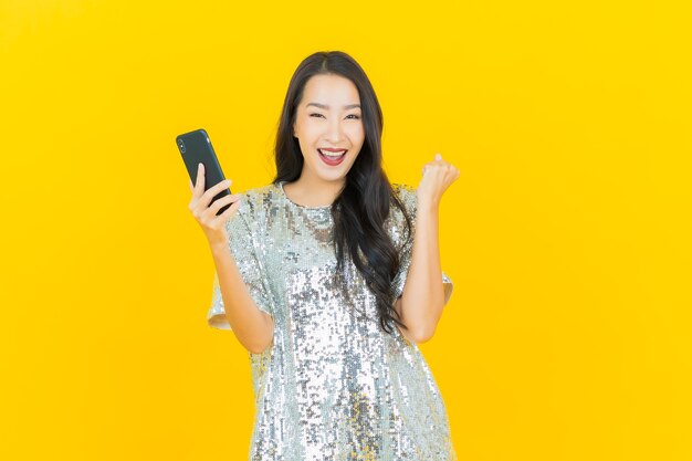 Portret piękna młoda azjatykcia kobieta uśmiech z inteligentny telefon komórkowy na żółto