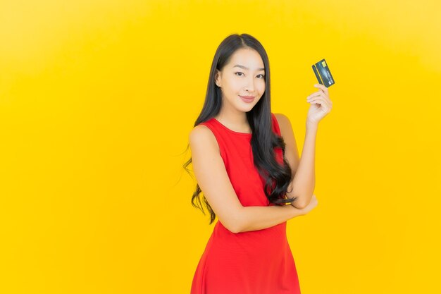 Portret piękna młoda azjatykcia kobieta uśmiech z kartą kredytową na żółtej ścianie