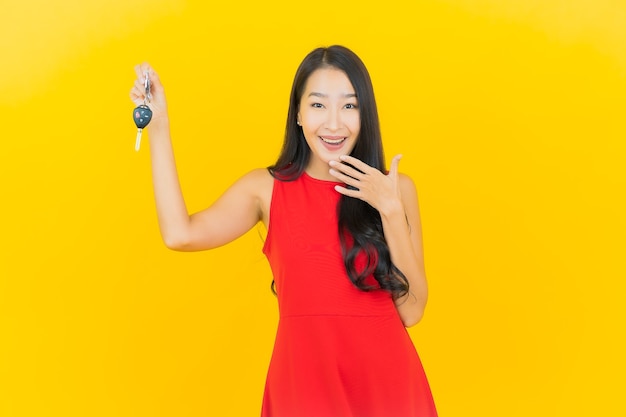 Portret piękna młoda azjatykcia kobieta uśmiech z kluczyk na żółtej ścianie