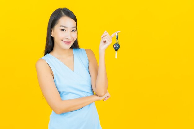 Portret piękna młoda azjatykcia kobieta uśmiech z kluczyk na żółtej ścianie