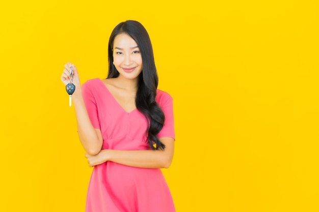 Portret piękna młoda azjatykcia kobieta uśmiecha się z kluczyk na żółtej ścianie