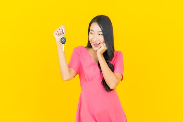 Portret piękna młoda azjatykcia kobieta uśmiecha się z kluczyk na żółtej ścianie