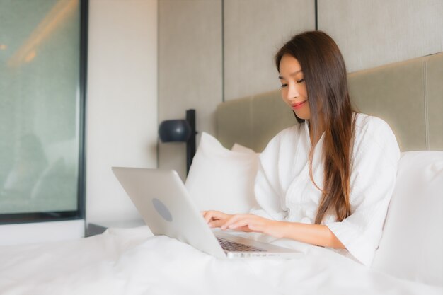 Portret piękna młoda azjatykcia kobieta używa laptop lub komputer w sypialni