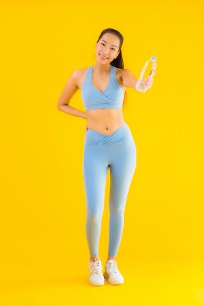Portret piękna młoda azjatykcia kobieta z butelki wodą na kolorze żółtym