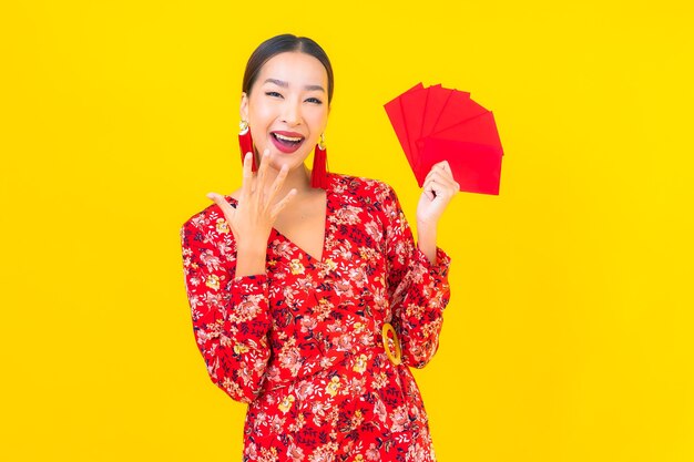 Portret piękna młoda azjatykcia kobieta z czerwonymi kopertami na żółtej ścianie